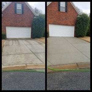 Side-by-side comparison of a double garage with a brick facade. The left image shows a concrete driveway with multiple stains and discolorations. The right image shows the same driveway, cleaned and uniformly bright. A green hose lies at the bottom.